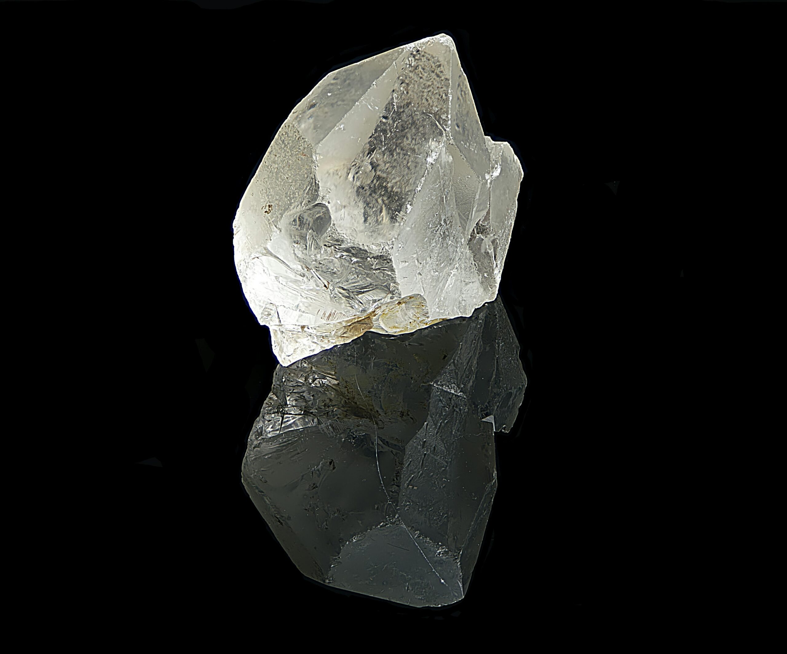 Clear quartz crystal with reflection against black background, showcasing natural beauty.